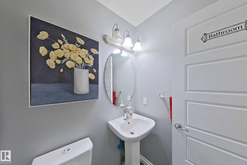 Bathroom featuring a pedestal sink with a mirror and vanity lighting, and a white paneled door - 1743 60 Street Sw, Edmonton, AB - Indoor Photo Showing Bathroom