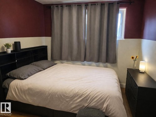 This room features a window with grey curtains, hardwood flooring, and a two-toned wall with a darker upper section - 13204 131A Avenue, Edmonton, AB - Indoor Photo Showing Bedroom