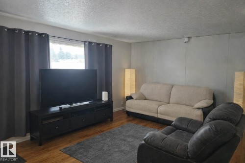 Living area featuring a window with dark curtains, wood flooring, and light grey walls - 13204 131A Avenue, Edmonton, AB - Indoor Photo Showing Living Room