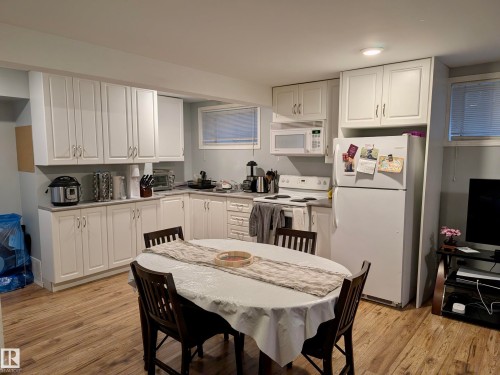 The kitchen features extensive white cabinetry, a white refrigerator, and a white oven with a matching microwave above - 10645 65 Avenue, Edmonton, AB - Indoor