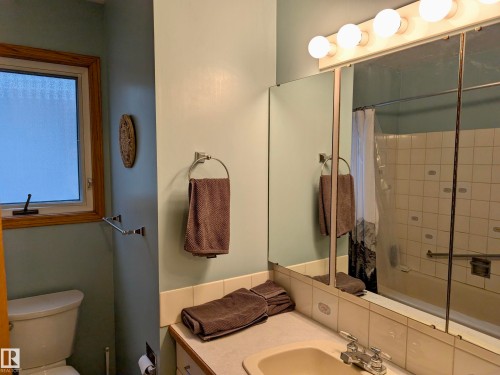 Bathroom featuring a window with wood trim, a vanity with a sink, a mirror, and a shower with a white tiled surround - 10645 65 Avenue, Edmonton, AB - Indoor Photo Showing Bathroom