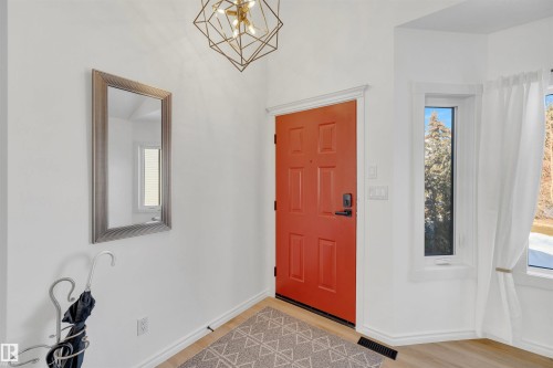 Welcoming entry with a vibrant orange front door, a decorative geometric light fixture, and a window with a view of natural surroundings - 131 West Liberty Crescent, Millet, AB - Indoor Photo Showing Other Room