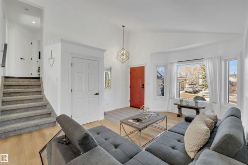 This living area features light wood flooring, a staircase with carpeted treads, and a prominent red entry door - 131 West Liberty Crescent, Millet, AB - Indoor Photo Showing Living Room