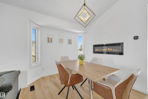 The dining area features light-toned flooring, a sleek wall-mounted fireplace, and a modern light fixture - 131 West Liberty Crescent, Millet, AB - Indoor Photo Showing Dining Room With Fireplace