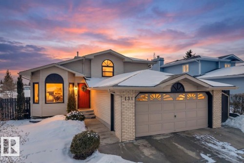 The property features a two-car garage with a decorative arch window, a red front door, and bay windows - 131 West Liberty Crescent, Millet, AB - Outdoor