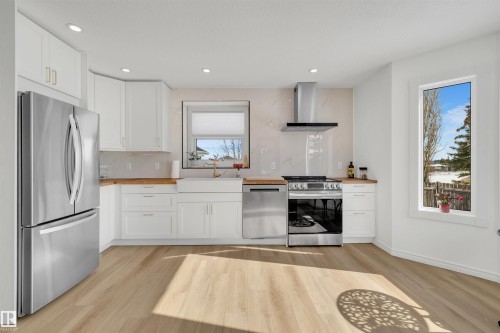 The kitchen features white cabinetry with gold-toned hardware, a stainless steel refrigerator, and a stainless steel range with an overhead range hood - 131 West Liberty Crescent, Millet, AB - Indoor Photo Showing Kitchen