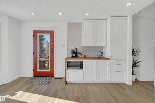 The property features light-colored flooring, a bright red door with a full-length glass panel, and white cabinetry with a light wood countertop - 131 West Liberty Crescent, Millet, AB - Indoor