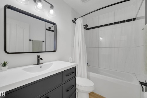 The bathroom features a vanity with a white countertop and a rectangular sink, a black framed mirror, and a shower/tub combination with white tile surround - 131 West Liberty Crescent, Millet, AB - Indoor Photo Showing Bathroom