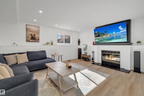 Living area featuring light wood flooring, a fireplace with a white brick surround and black hearth, and recessed lighting - 131 West Liberty Crescent, Millet, AB - Indoor Photo Showing Living Room With Fireplace