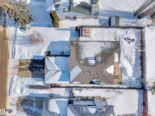 Aerial view of the property, showcasing its grey shingled roof, a paved driveway, and a fenced backyard with a fire pit area - 131 West Liberty Crescent, Millet, AB - Outdoor With View