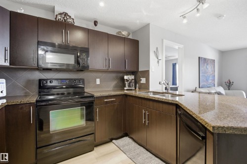 The kitchen features dark wood cabinetry, granite countertops, and stainless steel appliances including a built-in microwave and an electric range - 115 2208 44 Avenue, Edmonton, AB - Indoor Photo Showing Kitchen With Double Sink