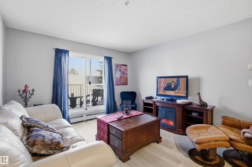 The living area features a light-toned flooring, a sliding glass door with blue curtains leading to an outdoor space, and light-colored walls - 115 2208 44 Avenue, Edmonton, AB - Indoor Photo Showing Living Room