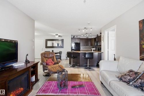 Open concept living area featuring light-colored flooring, neutral wall tones, and track lighting in the kitchen - 115 2208 44 Avenue, Edmonton, AB - Indoor Photo Showing Living Room