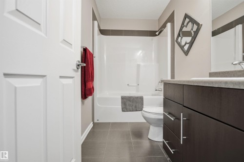 The bathroom features a sleek vanity with a countertop sink, a full-size mirror, and a white tub with an integrated shower - 115 2208 44 Avenue, Edmonton, AB - Indoor Photo Showing Bathroom