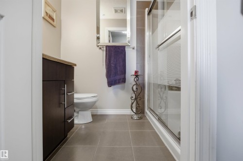 Bathroom featuring a dark wood vanity with a light-colored countertop, a toilet, a shower with a clear and textured glass door, and tiled flooring - 115 2208 44 Avenue, Edmonton, AB - Indoor Photo Showing Bathroom