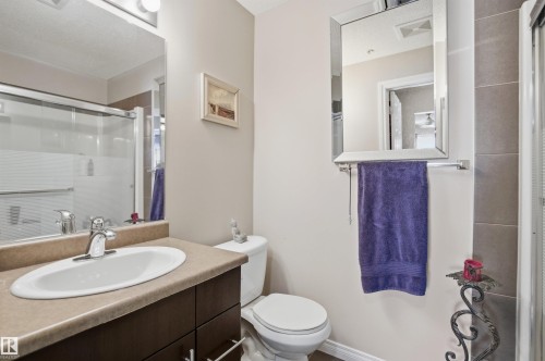 The bathroom features a vanity with an integrated sink, a mirror with an overhead light fixture, and a shower with a sliding glass door - 115 2208 44 Avenue, Edmonton, AB - Indoor Photo Showing Bathroom