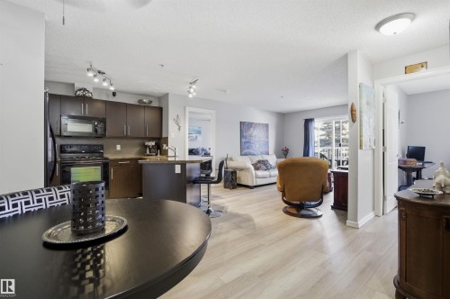 The property features an open-concept living area with light-toned flooring, a kitchen with dark cabinetry and black appliances, and a balcony visible through large glass doors - 115 2208 44 Avenue, Edmonton, AB - Indoor