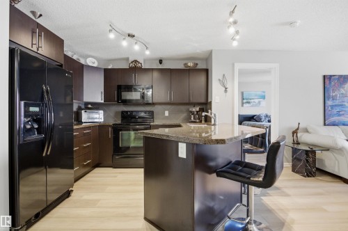 The kitchen features dark wood cabinetry, a granite countertop, and stainless steel appliances - 115 2208 44 Avenue, Edmonton, AB - Indoor Photo Showing Kitchen With Upgraded Kitchen