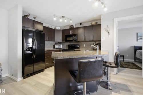 The kitchen features dark wood cabinetry, a granite countertop, and track lighting - 115 2208 44 Avenue, Edmonton, AB - Indoor Photo Showing Kitchen
