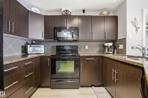 The kitchen features dark wood cabinetry, granite countertops, and a tile backsplash - 115 2208 44 Avenue, Edmonton, AB - Indoor Photo Showing Kitchen With Double Sink