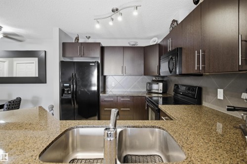 Kitchen featuring granite countertops, dark wood cabinetry, stainless steel sink, and black appliances - 115 2208 44 Avenue, Edmonton, AB - Indoor Photo Showing Kitchen With Double Sink With Upgraded Kitchen