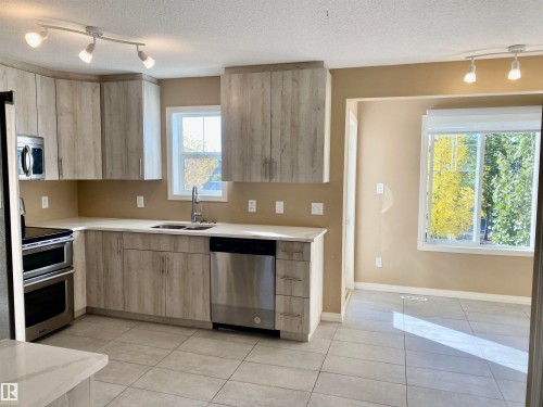Kitchen featuring rail lighting, light wood finish cabinetry, stainless steel appliances, light tile patterned floors, and a textured ceiling - 403 178 Bridgeport Boulevard, Leduc, AB - Indoor Photo Showing Kitchen With Double Sink