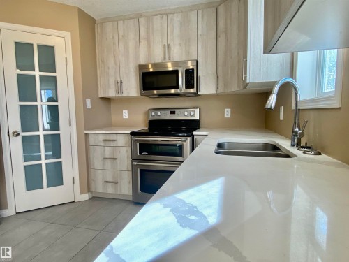 Kitchen with stainless steel appliances, light stone counters, light wood finish cabinets, modern cabinets, and light tile patterned floors - 403 178 Bridgeport Boulevard, Leduc, AB - Indoor Photo Showing Kitchen With Stainless Steel Kitchen With Double Sink