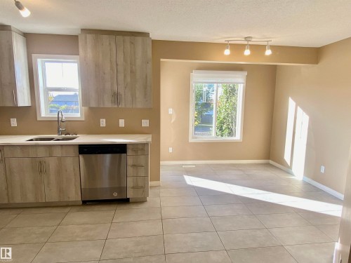 Kitchen with light wood finish cabinetry, dishwasher, modern cabinets, light tile patterned floors, and a textured ceiling - 403 178 Bridgeport Boulevard, Leduc, AB - Indoor