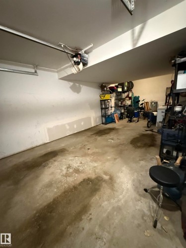The property includes a spacious garage with a concrete floor, an overhead garage door opener, and white painted walls - 403 178 Bridgeport Boulevard, Leduc, AB - Indoor Photo Showing Garage
