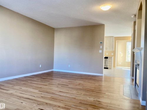 Spare room featuring a fireplace, light wood-style floors, and a textured ceiling - 403 178 Bridgeport Boulevard, Leduc, AB - Indoor Photo Showing Other Room