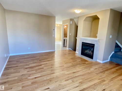 Unfurnished living room with a glass covered fireplace and light wood-style floors - 403 178 Bridgeport Boulevard, Leduc, AB - Indoor Photo Showing Living Room With Fireplace