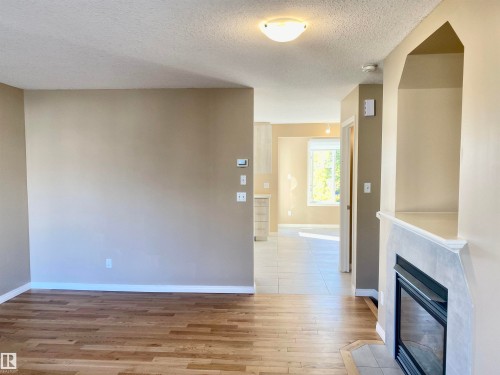 Unfurnished living room featuring a tile fireplace, a textured ceiling, and light wood-style floors - 403 178 Bridgeport Boulevard, Leduc, AB - Indoor Photo Showing Other Room With Fireplace