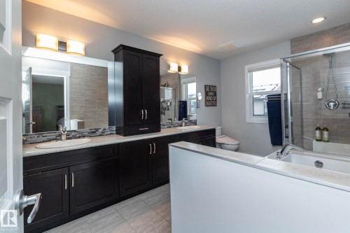 The bathroom features a dual vanity with dark cabinetry, light countertops, and individual mirrors with modern light fixtures - 7608 179 Avenue, Edmonton, AB - Indoor Photo Showing Bathroom