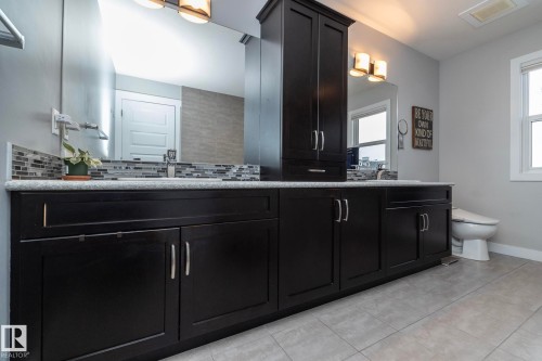 Bathroom vanity featuring dark wood cabinetry, a light-colored countertop, and a mosaic tile backsplash - 7608 179 Avenue, Edmonton, AB - Indoor Photo Showing Bathroom