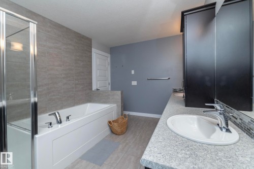 The bathroom features a built-in bathtub with tiled surround, a shower with glass enclosure, a vanity with an integrated sink, and an overhead mirror - 7608 179 Avenue, Edmonton, AB - Indoor Photo Showing Bathroom