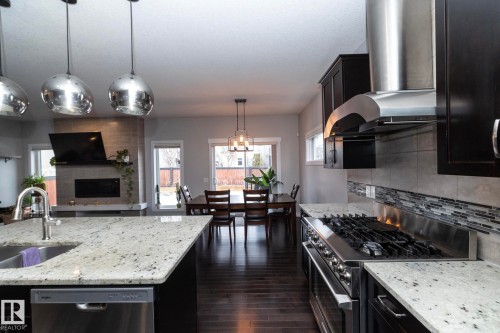 The kitchen features granite countertops, dark cabinetry, and stainless steel appliances including a range hood and dishwasher - 7608 179 Avenue, Edmonton, AB - Indoor Photo Showing Kitchen With Upgraded Kitchen