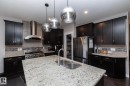 The kitchen features dark wood cabinetry, stainless steel appliances, a large center island with a sink, and pendant lighting - 7608 179 Avenue, Edmonton, AB  - Indoor Photo Showing Kitchen With Double Sink 