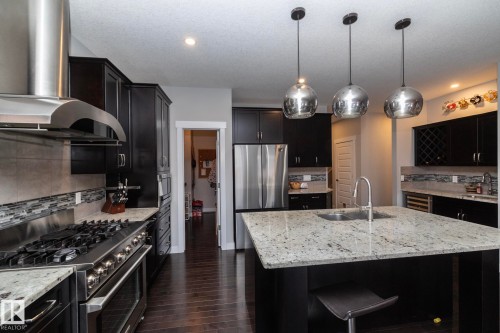 The kitchen features dark wood cabinets, stainless steel appliances, and a large central island with a sink and light-colored granite countertops - 7608 179 Avenue, Edmonton, AB - Indoor Photo Showing Kitchen With Double Sink With Upgraded Kitchen