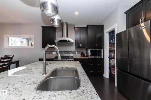 Well-appointed kitchen featuring granite countertops, a stainless steel sink with a gooseneck faucet, dark wood cabinetry, and stainless steel appliances - 7608 179 Avenue, Edmonton, AB - Indoor Photo Showing Kitchen With Double Sink With Upgraded Kitchen