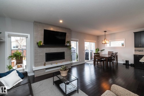 Open concept living area featuring dark hardwood floors, a stone-tiled fireplace, and a sliding glass door leading to the exterior - 7608 179 Avenue, Edmonton, AB - Indoor Photo Showing Living Room