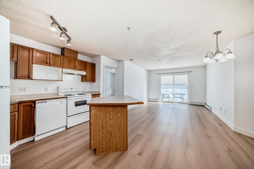 The kitchen features wood cabinetry, white appliances, and an island with a light-colored countertop - 126 16221 95 Street, Edmonton, AB - Indoor Photo Showing Kitchen