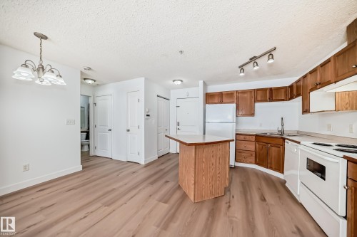 The open-concept living area features light wood-style flooring, a kitchen with wood cabinetry and white appliances, and a light-colored kitchen island with a countertop - 126 16221 95 Street, Edmonton, AB - Indoor Photo Showing Kitchen