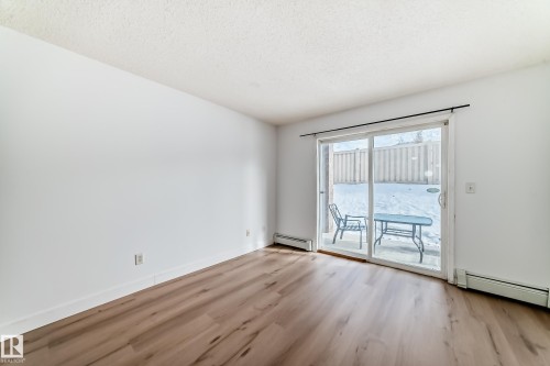 The property features light wood flooring, white walls, and a sliding glass door providing access to an outdoor patio area - 126 16221 95 Street, Edmonton, AB - Indoor Photo Showing Other Room