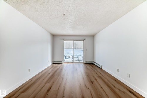 Open concept living area with light wood-style flooring and white walls, offering access to an outdoor patio through sliding glass doors - 126 16221 95 Street, Edmonton, AB - Indoor Photo Showing Other Room