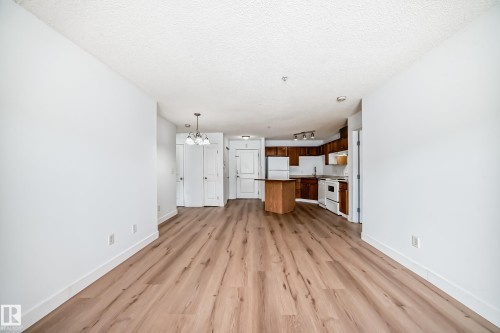 This open-concept living area features light wood-style flooring and white walls, with a kitchen visible in the background - 126 16221 95 Street, Edmonton, AB - Indoor