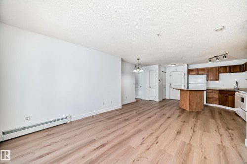 This property features light wood flooring, white walls, and a kitchen with wooden cabinetry, a white refrigerator, and a white oven - 126 16221 95 Street, Edmonton, AB - Indoor Photo Showing Kitchen