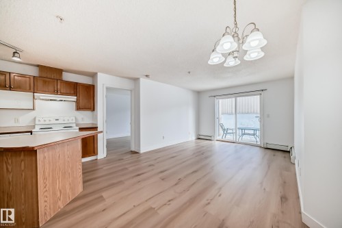 This inviting living space features light wood-look flooring, a chandelier with white shades, and a sliding glass door leading to a patio - 126 16221 95 Street, Edmonton, AB - Indoor Photo Showing Kitchen