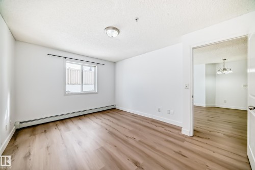 The property features light-toned wood-style flooring and bright white walls, enhancing the natural light from the window - 126 16221 95 Street, Edmonton, AB - Indoor Photo Showing Other Room
