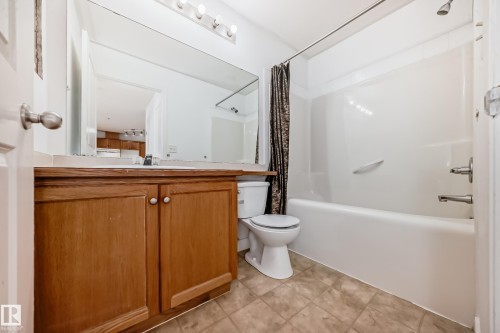 The bathroom features a vanity with wooden cabinetry and a light-colored countertop, a white toilet, and a white bathtub with a showerhead and metal fixtures - 126 16221 95 Street, Edmonton, AB - Indoor Photo Showing Bathroom
