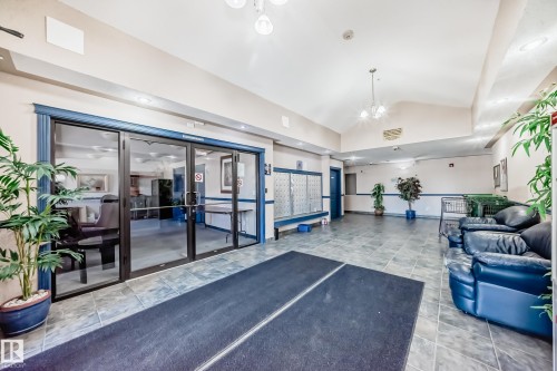 The building features a spacious common area with tiled flooring, vaulted ceilings, and a seating area with blue leather sofas - 126 16221 95 Street, Edmonton, AB - Indoor Photo Showing Other Room